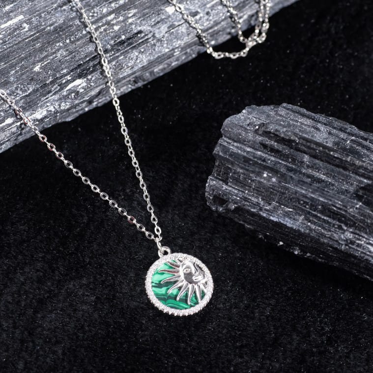 "Radiant emerald pendant surrounded by sunburst rays in a bold design"